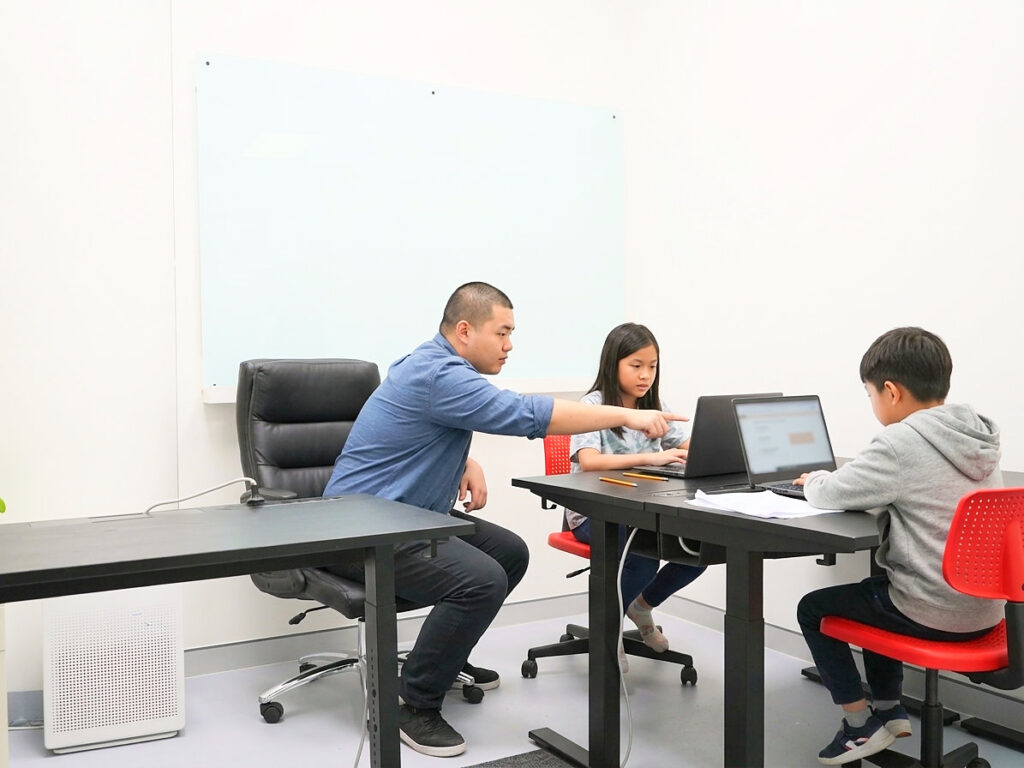 OC & Selective A tutor guiding two primary school students through practice questions on laptops