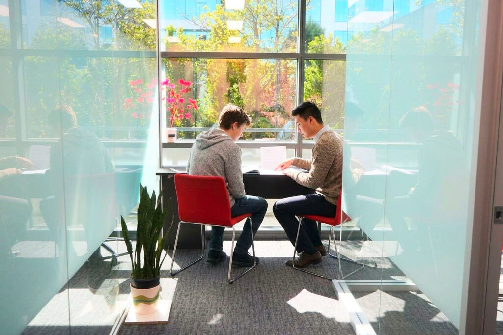 A tutor and a senior student reviewing an essay at a desk by a sunny window